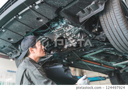 A male mechanic/service technician working, inspecting and servicing the underside of a car that has been lifted 124497924