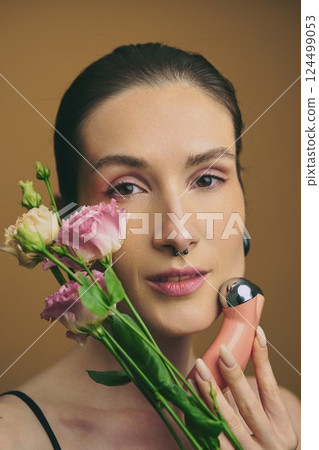 Woman holding flowers and beauty tool during indoor wellness session 124499053
