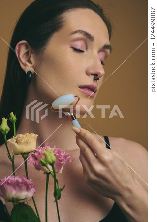 Woman using facial roller while surrounded by colorful flowers indoors 124499087