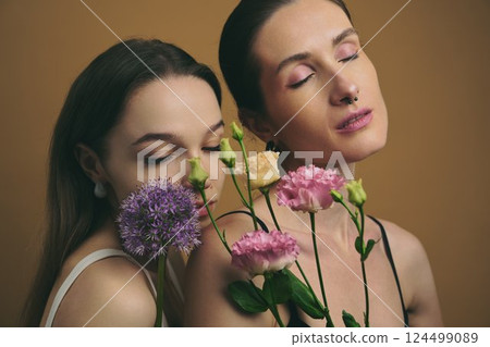 Two women posing with flowers in a studio setting 124499089