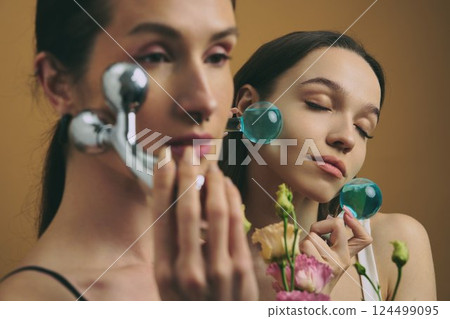 Women using facial rollers while surrounded by flowers in a serene setting Women using facial rollers while surrounded by flowers in a serene setting 124499095
