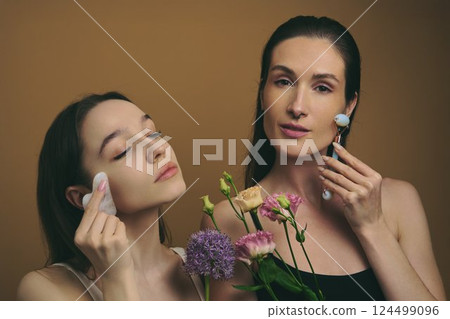 Women applying skincare while holding flowers in a serene setting 124499096