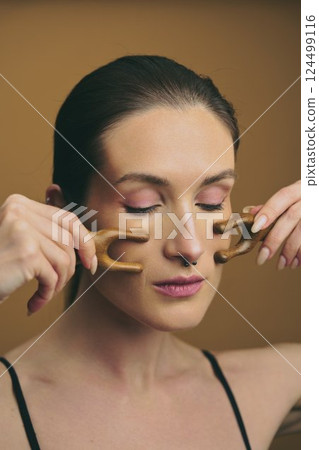 Woman practicing facial massage technique with wooden tools for relaxation Woman practicing facial massage technique with wooden tools for relaxation 124499116