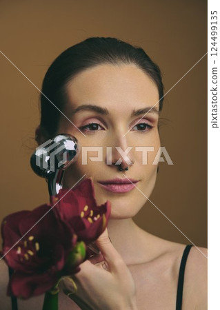 Woman using a facial massager with flowers in a studio setting 124499135