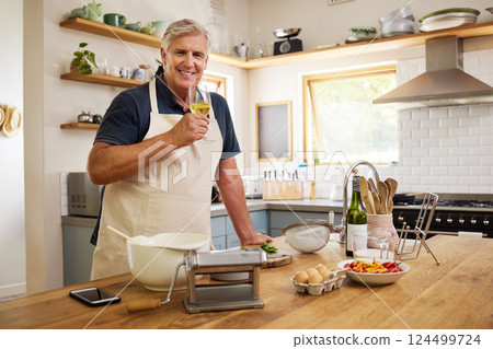 Elderly man drinking wine while cooking in kitchen for date, dinner or lunch in his home. Happy, smile and senior guy in retirement enjoying glass of alcohol beverage while preparing food at a house. 124499724