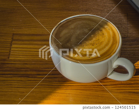 Warm coffee resting on a wooden table with sunlight streaming in Warm coffee resting on a wooden table with sunlight streaming in 124501515
