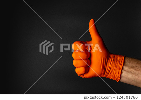 Gloved hand giving a thumbs up against dark background 124501760