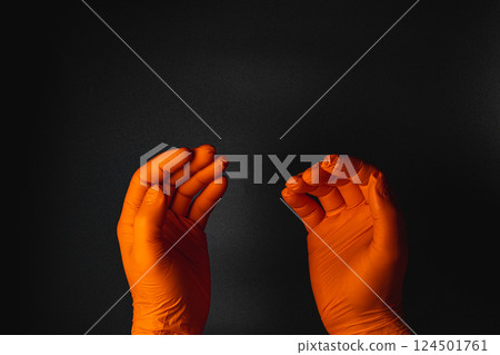 Hands wearing orange gloves against a black background 124501761