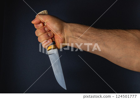Hand gripping a knife against a dark background 124501777