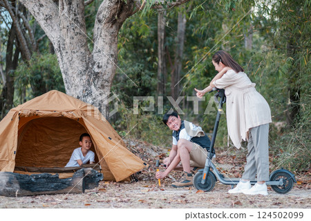 A family camping in the forest, featuring a tent and a scooter, enjoying nature and outdoor activities. 124502099