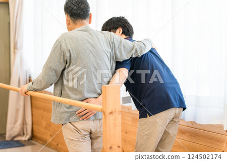 Senior man using handrails for walking training, accompanied by an occupational therapist and male physical therapist 124502174