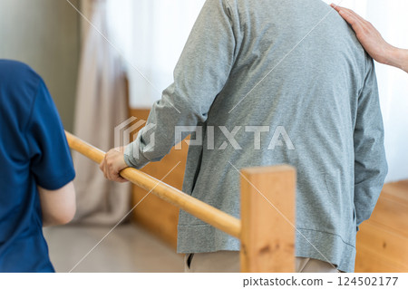 老年男子利用扶手進行步行訓練,由職能治療師和男性物理治療師陪同 老年男子利用扶手進行步行訓練,由職能治療師和男性物理治療師陪同 124502177