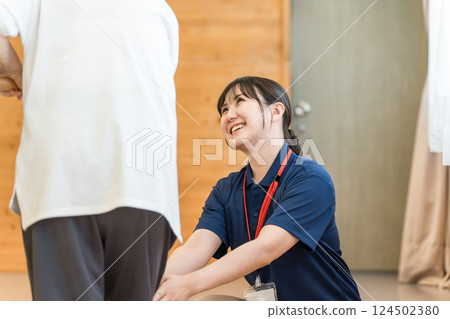 一名老年婦女在一名職業治療師和一名女性物理治療師的陪同下使用扶手訓練行走技能 124502380
