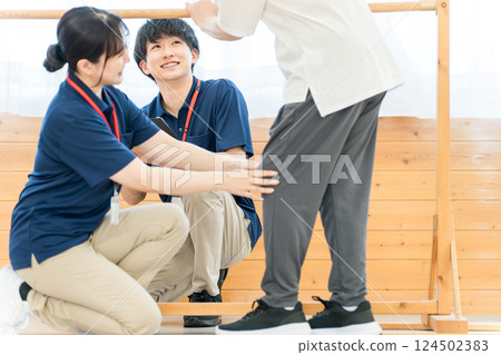 老年婦女使用扶手進行步行訓練，男女職能治療師和物理治療師工作人員協助她 124502383