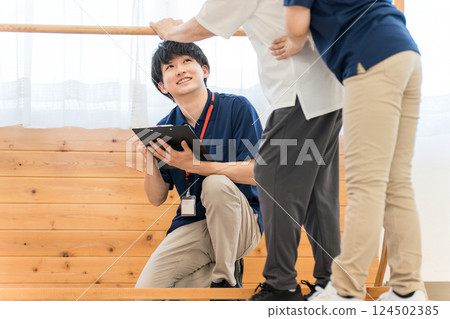 Senior woman using handrails for walking training and male and female occupational therapist and physiotherapist staff assisting her 124502385