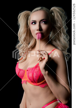 Woman in bright lingerie holding a candy lollipop against a dark background Woman in bright lingerie holding a candy lollipop against a dark background 124502526