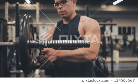 The male athlete changes the weight on the barbell. The male athlete changes the weight on the barbell. 124503567