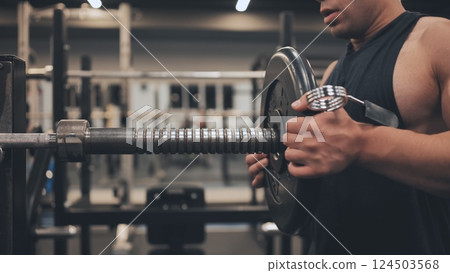 The male athlete changes the weight on the barbell. The male athlete changes the weight on the barbell. 124503568