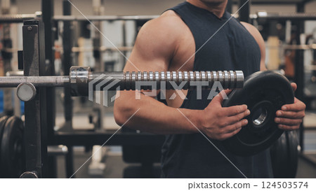 The male athlete changes the weight on the barbell. The male athlete changes the weight on the barbell. 124503574
