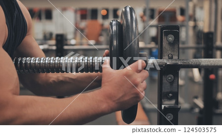 The male athlete changes the weight on the barbell. The male athlete changes the weight on the barbell. 124503575
