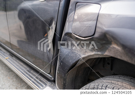 Car body damage near wheel well and fuel cap from collision or impact, showing dents and scratches on black vehicle surface. 124504105