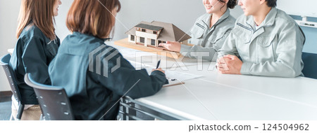 Male and female businessmen in the construction and building industry wearing work clothes negotiating, explaining and presenting using a house model 124504962