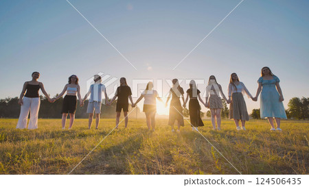 Young students linking hands in a field, savoring the summer sunset during a break 124506435