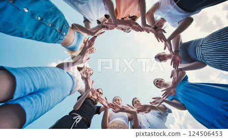 School friends uniting in a circle with their hands, demonstrating teamwork, unity, and friendship under a clear blue sky 124506453
