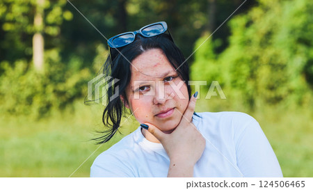 Young woman with sunglasses is touching her chin with her hand, enjoying a sunny day at the park 124506465