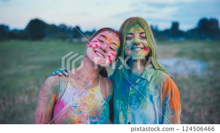 Two young women, covered in vibrant holi powder paint, embrace and smile, celebrating friendship and the joy of the festival 124506466