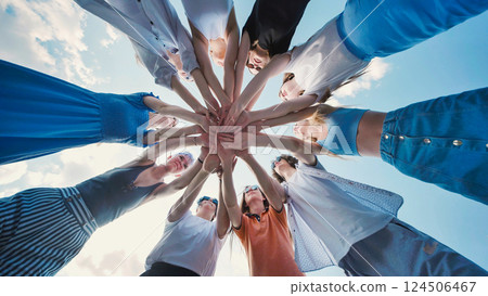 School friends standing in a circle, linking hands against a blue sky, representing unity, teamwork, and collaboration 124506467