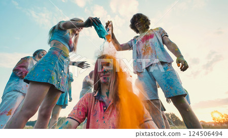 School friends joyfully throwing colorful gulal powder on classmate during holi festival celebration at sunset School friends joyfully throwing colorful gulal powder on classmate during holi festival celebration at sunset 124506494