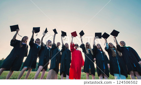 Graduates joyfully throwing mortarboards in the air to celebrate academic success at sunset 124506502