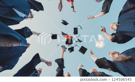 Graduates in academic attire tossing their caps in the air against a clear blue sky, rejoicing in their academic success 124506545
