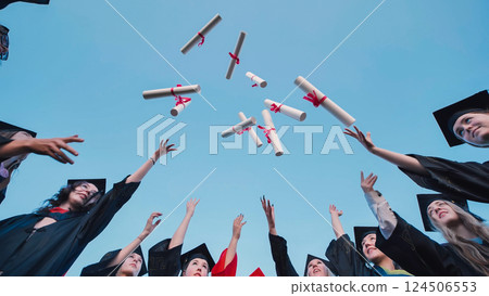 Students in graduation attire tossing their diplomas in the air, rejoicing in their academic success 124506553