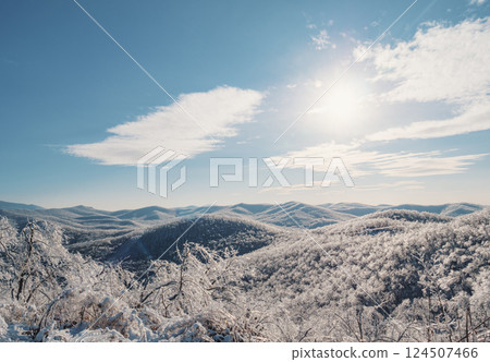 Winter landscape showcases snow-covered hills under a bright blue sky and radiant sun in serene mountain setting Winter landscape showcases snow-covered hills under a bright blue sky and radiant sun in serene mountain setting 124507466