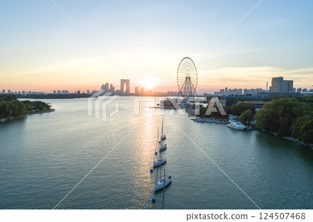 Sunset view over the river with a ferris wheel and sailboats in the foreground 124507468