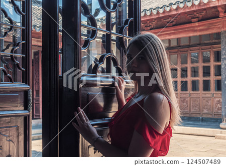 A young woman in a red dress stands at an ornate wooden door. A young woman in a red dress stands at an ornate wooden door. 124507489