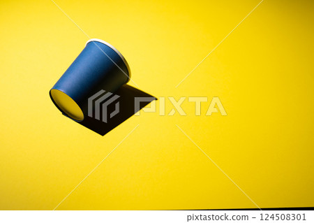 Cardboard coffee cup in blue on a yellow background with a shadow. 124508301