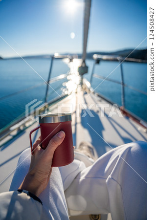 Woman hands holding thermo mug sitting on bow of the yacht during sailing in the morning in winter time in Adriatic sea, relaxation in yachting time Woman hands holding thermo mug sitting on bow of the yacht during sailing in the morning in winter time in Adriatic sea, relaxation in yachting time 124508427