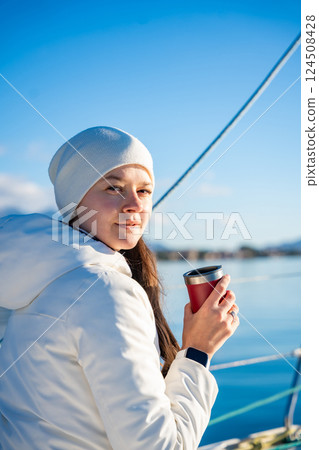 Woman hands holding thermo mug sitting on bow of the yacht during sailing in the morning in winter time in Adriatic sea, relaxation in yachting time Woman hands holding thermo mug sitting on bow of the yacht during sailing in the morning in winter time in Adriatic sea, relaxation in yachting time 124508428