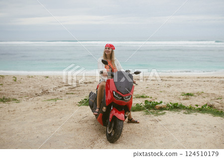 Attractive caucasian woman in a bikini swimsuit and on a bike scooter near the beach in sunny weather. 124510179