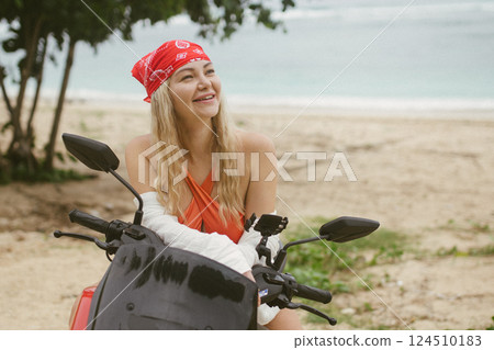 Attractive caucasian woman in a bikini swimsuit and on a bike scooter near the beach in sunny weather. 124510183