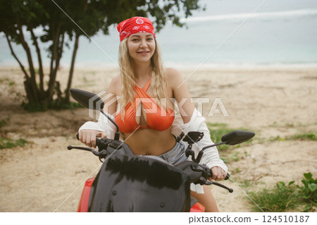Attractive caucasian woman in a bikini swimsuit on a bike scooter near the beach in sunny weather. Attractive caucasian woman in a bikini swimsuit on a bike scooter near the beach in sunny weather. 124510187