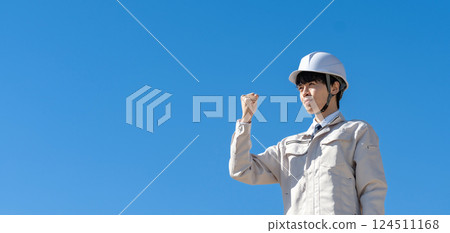 Young man in work clothes, blue sky, fist pump 124511168