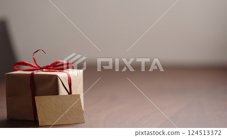Slide tracking shot of brown paper gift box with red bow on wood table with blank paper card 124513372