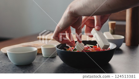 man put feta cheese into greek salad in black bowl 124513381