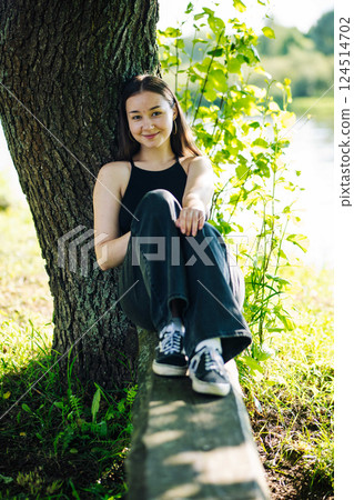 Student relaxing under tree, absorbing peaceful park surroundings with calm demeanor Student relaxing under tree, absorbing peaceful park surroundings with calm demeanor 124514702