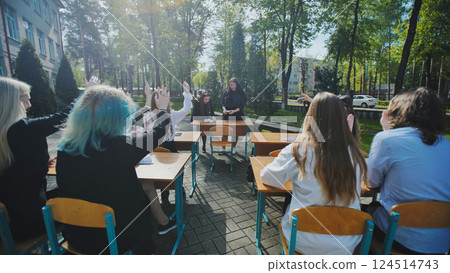 High school students raising hands to answer teacher's question during open air lesson in schoolyard High school students raising hands to answer teacher's question during open air lesson in schoolyard 124514743