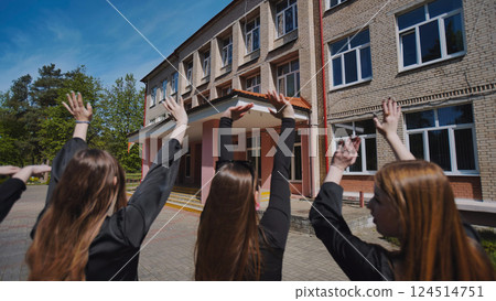 Students graduating and celebrating in front of school building, excited for the future ahead 124514751